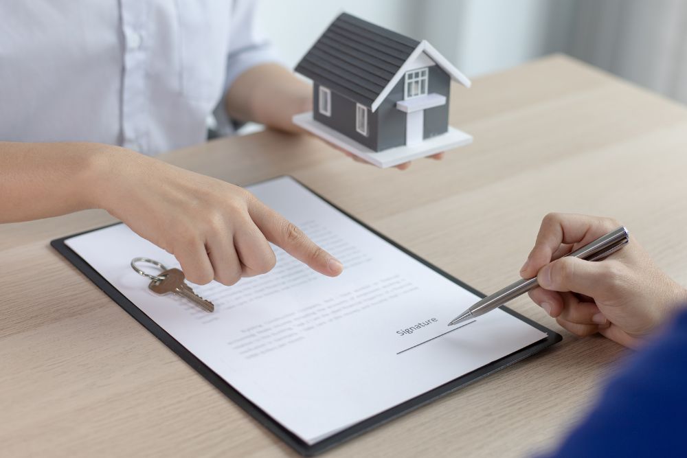 Homeowners vs Renters Insurance comparison during policy signing with home model, keys, and insurance paperwork