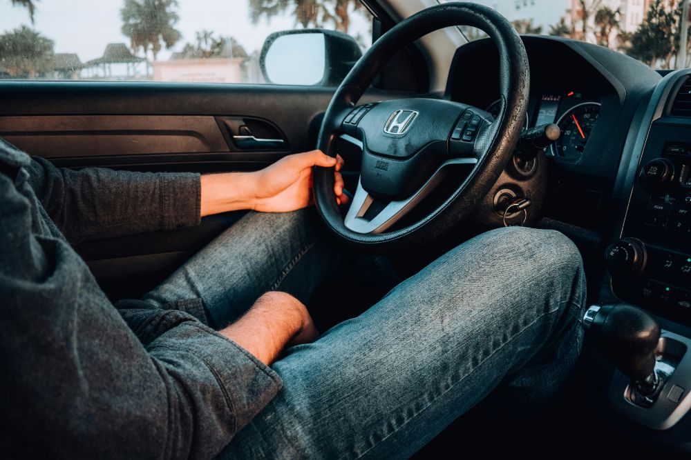 Close-up view of a person driving a car, with one hand on the steering wheel and the dashboard and center console visible, representing everyday personal auto insurance coverage.