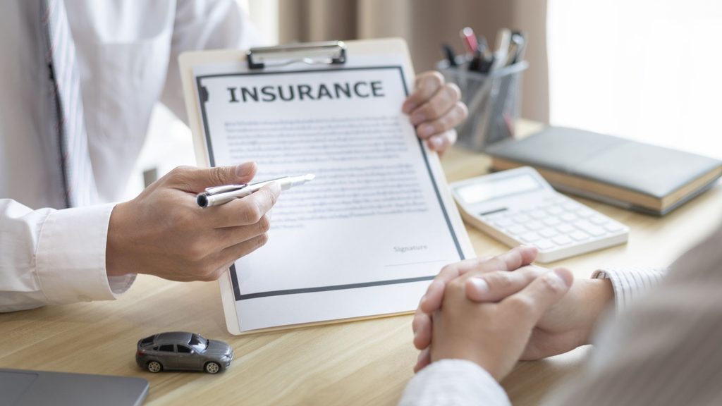 Two people reviewing an insurance form on a clipboard, with a toy car on the desk