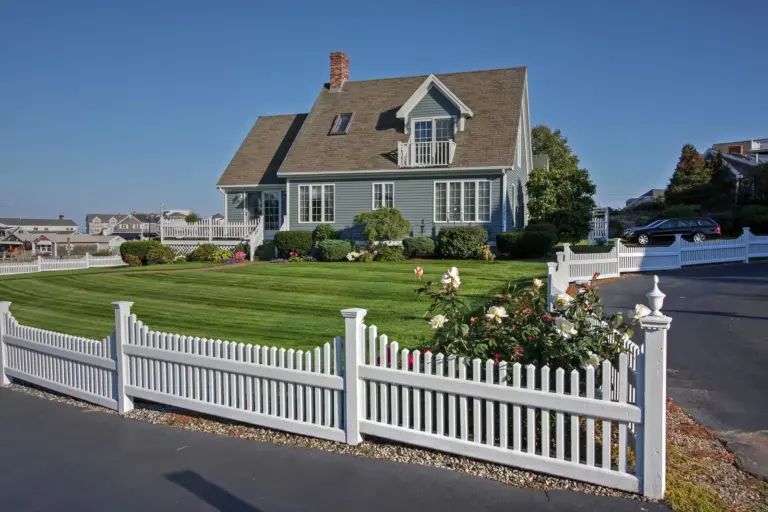 Blue-gray Cape-style coastal New England home with a manicured lawn and a white picket fence
