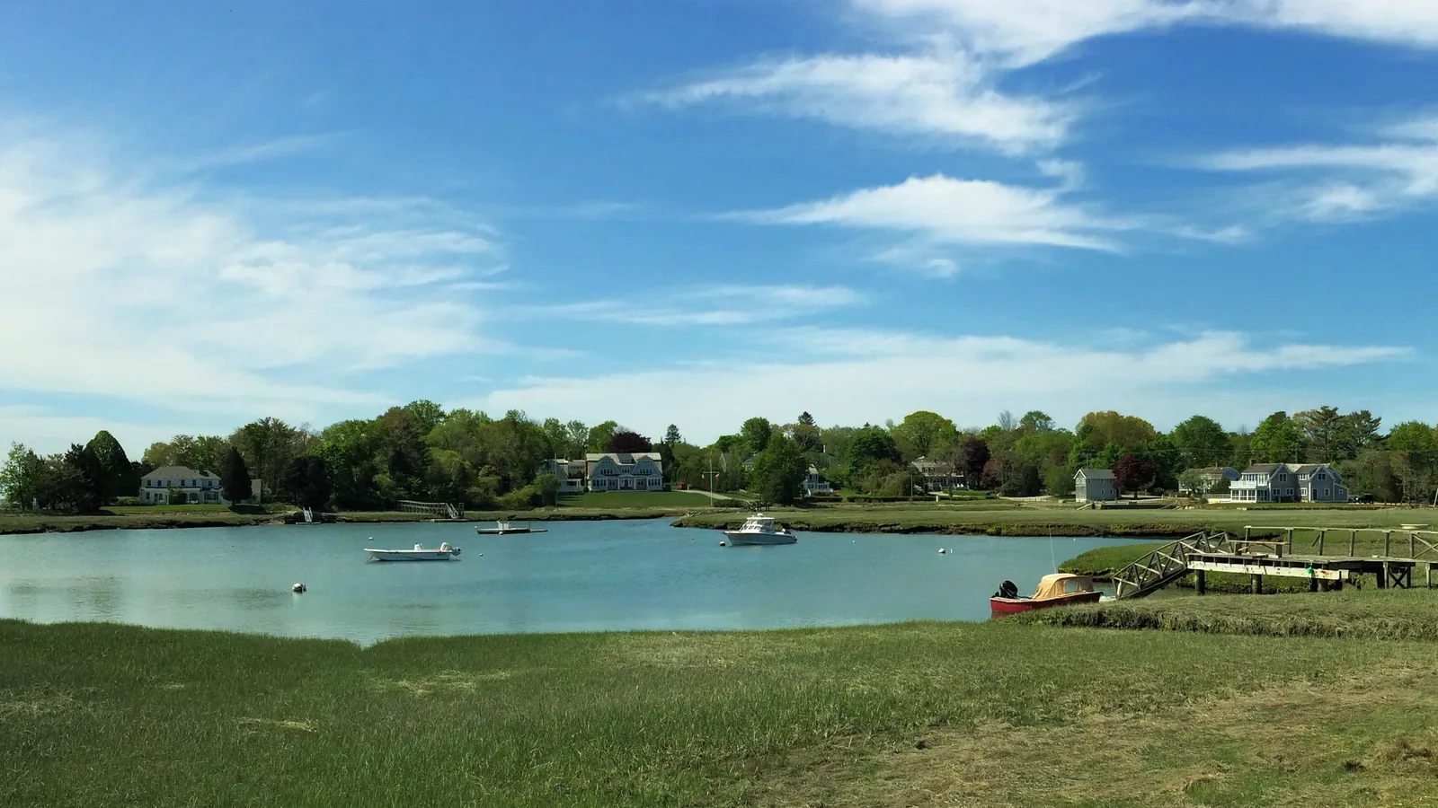 Waterfront homes above the salt marsh along the Bluefish River estuary in Duxbury, with small boats on moorings and a wooden dock