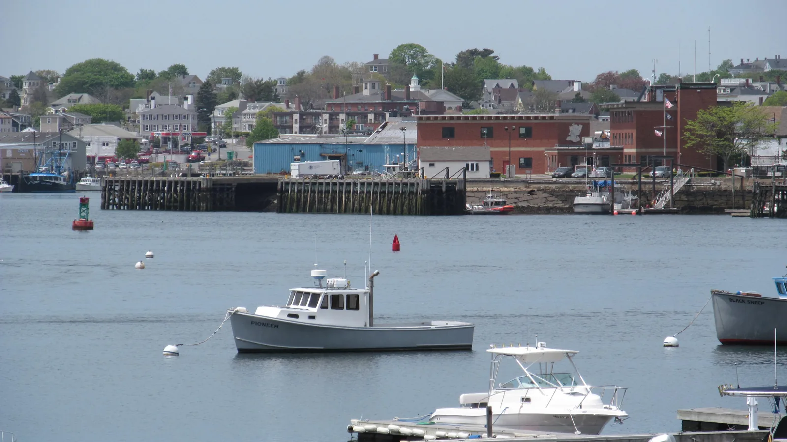 Homes on the hillside above Gloucester Harbor in Gloucester, Massachusetts, with waterfront piers and boats on moorings in the foreground