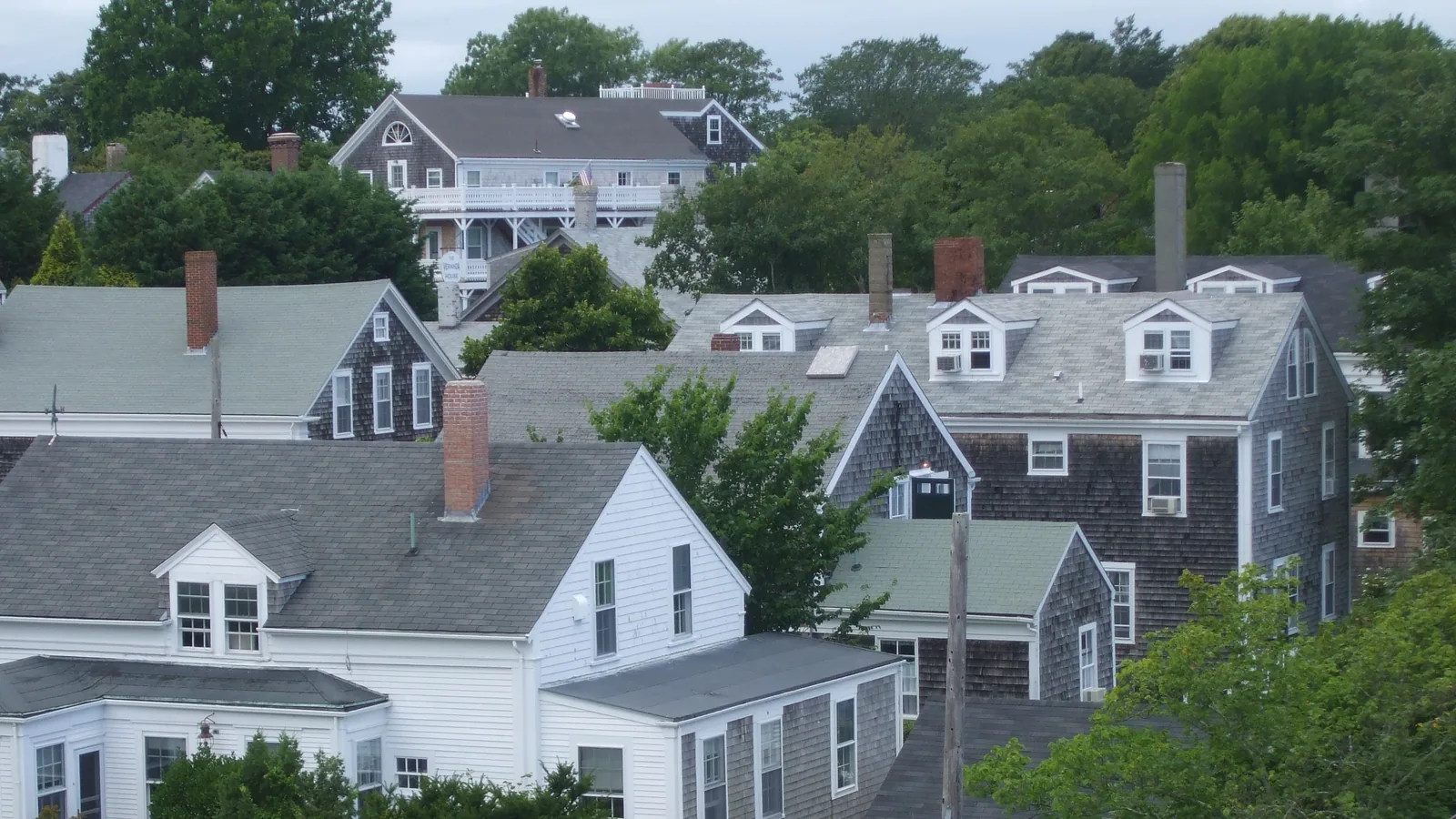 Cedar-shingled and white clapboard houses with brick chimneys and dormers in Nantucket town, seen from above the rooftops