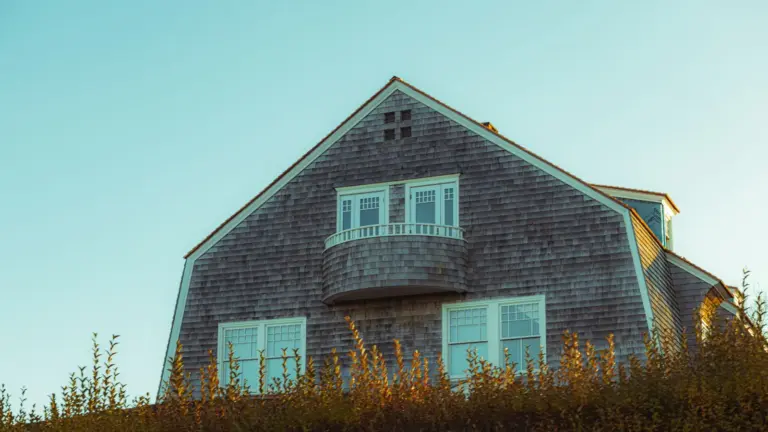 Cedar-shingled coastal house with a curved balcony under a clear sky in New England