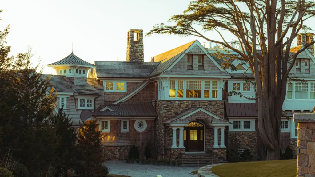 Large stone and shingle-style estate home with a turret and copper accents at sunset in New England