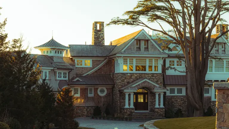 Large stone and shingle-style estate home with a turret and copper accents at sunset in New England
